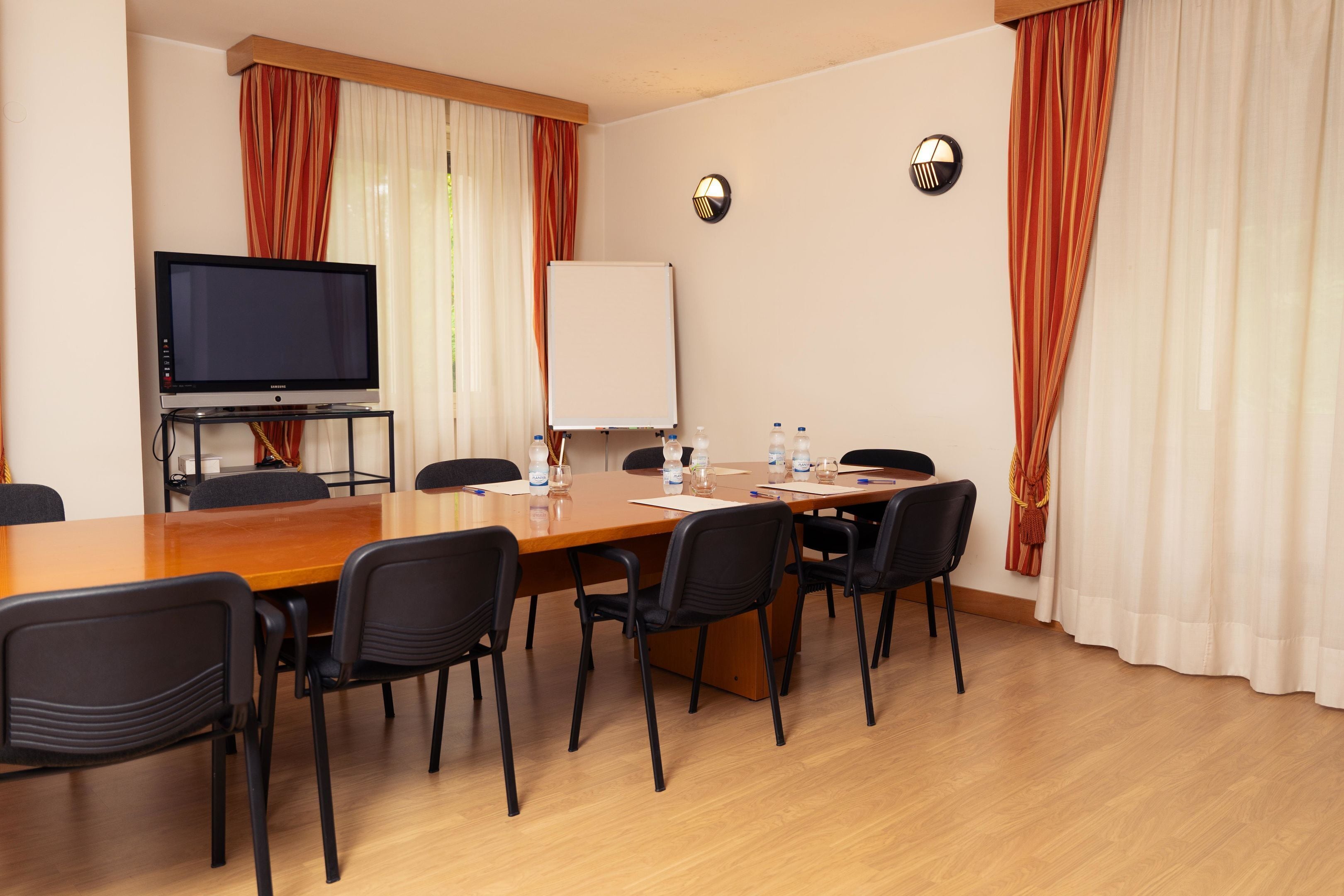 A conference room with a wooden table, black chairs, a television, a whiteboard, and two clocks on the wall.