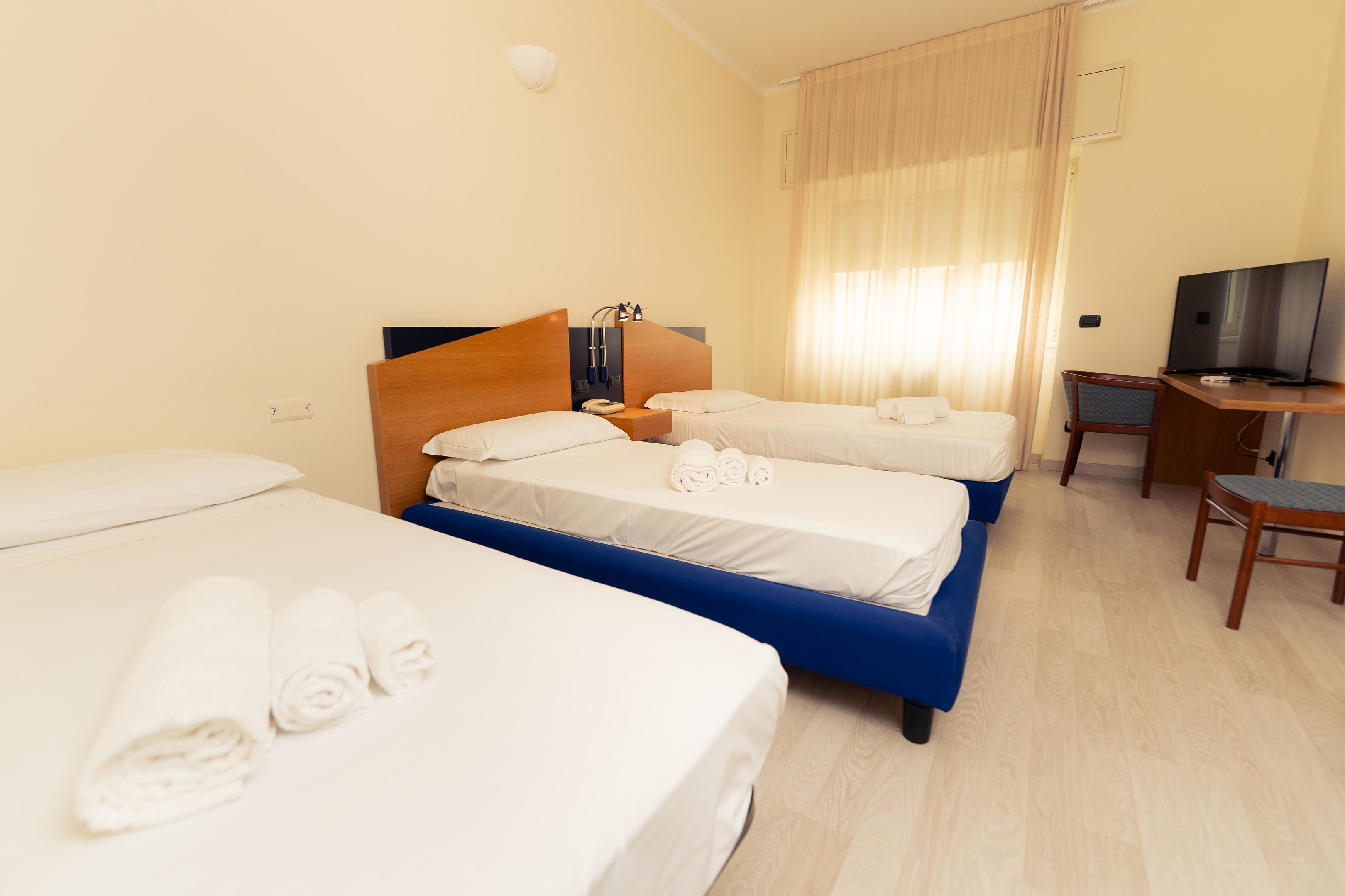 A hotel room with three beds, a desk, a television, and a chair.