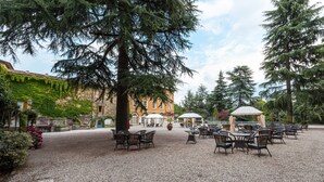 An outdoor patio area with tables and chairs, surrounded by trees and a building with ivy-covered walls. - Hotel San Pancrazio (Trescore Balneario)