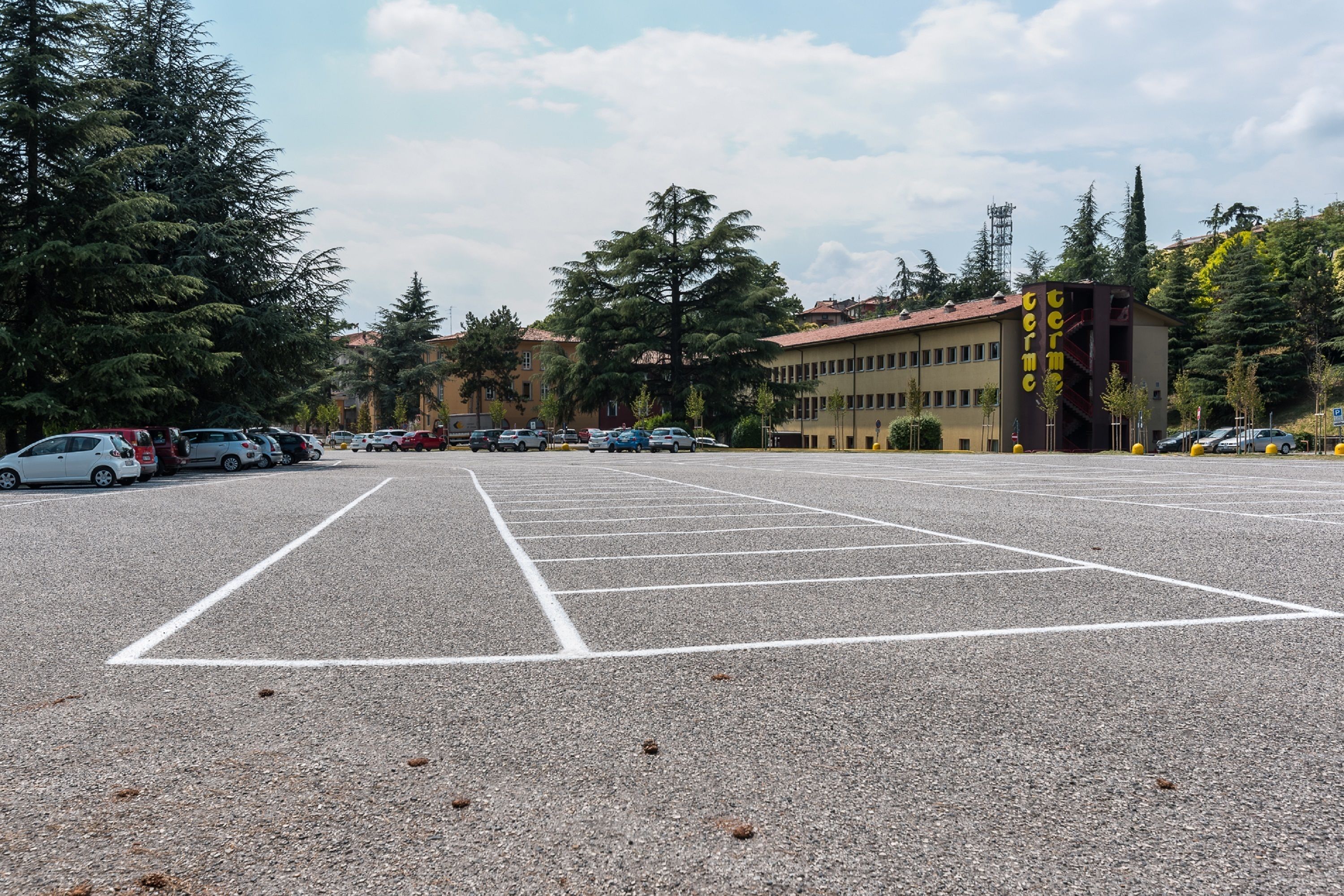 Un estacionamiento con espacios delimitados, rodeado de árboles y edificios.