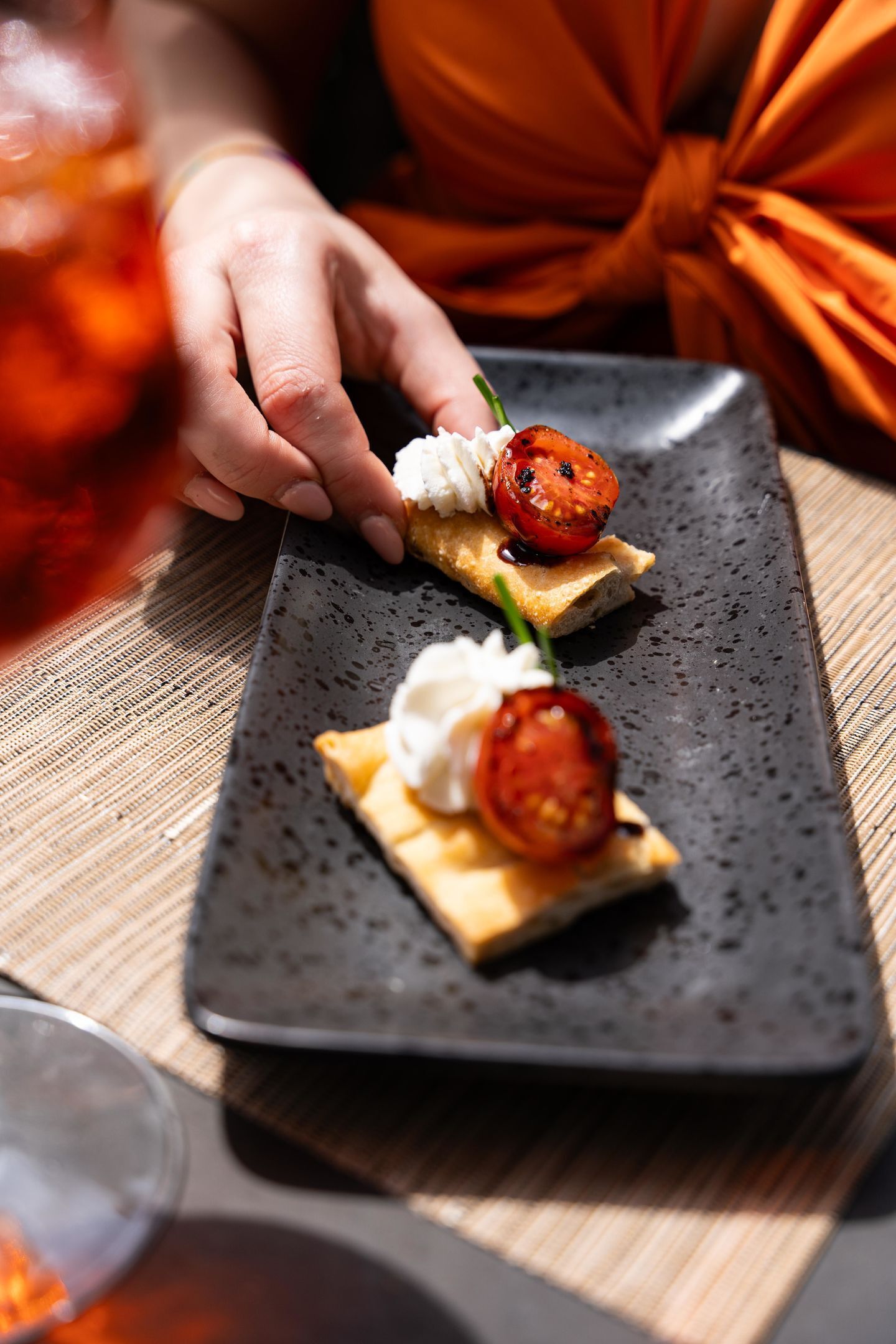 A rectangular plate with three small sandwiches, each topped with a slice of tomato and a dollop of cream.
