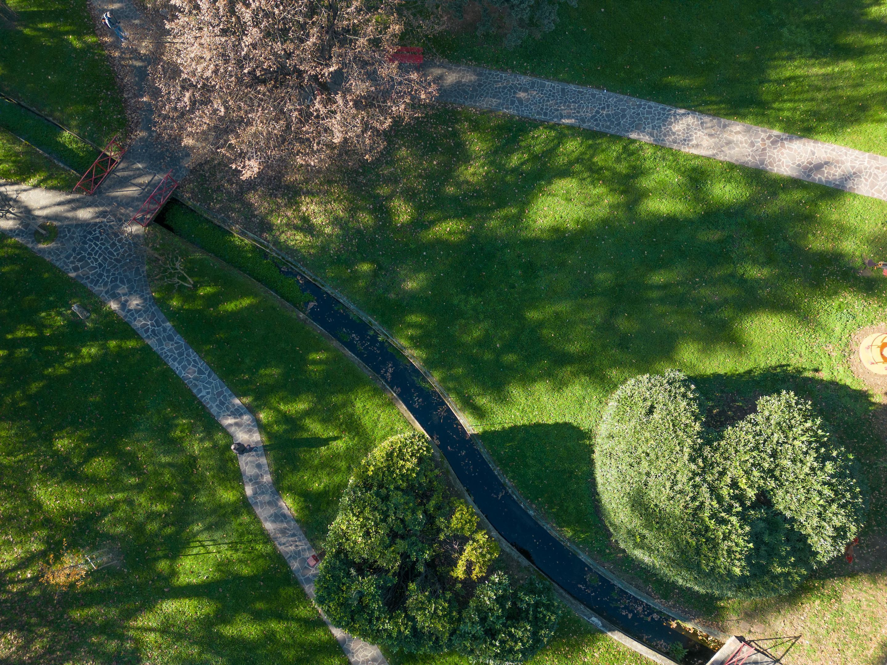 An aerial view of a park with a paved walkway, a circular garden, and a tree-lined path.