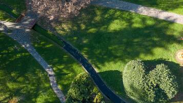 An aerial view of a park with a paved walkway, a circular garden, and a tree-lined path.