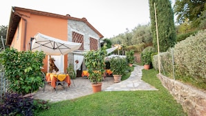 A patio area with stone flooring, outdoor tables with orange tablecloths, and potted plants.