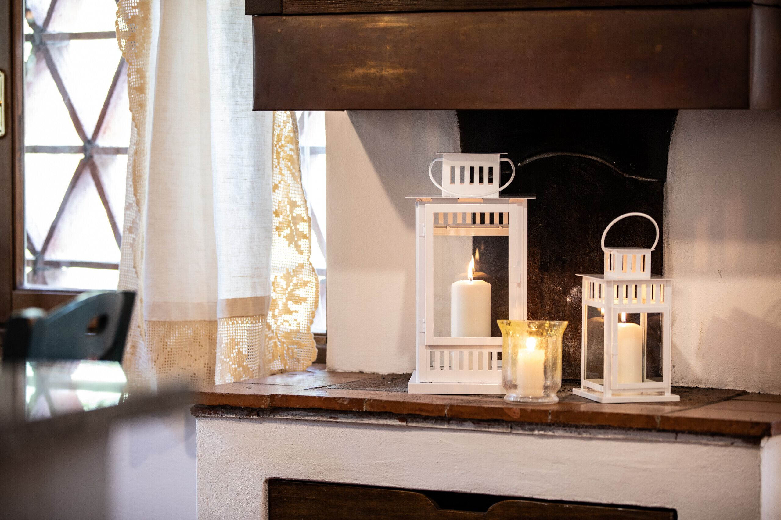 Une cheminée surmontée d’une étagère décorée de lanternes blanches et de bougies.