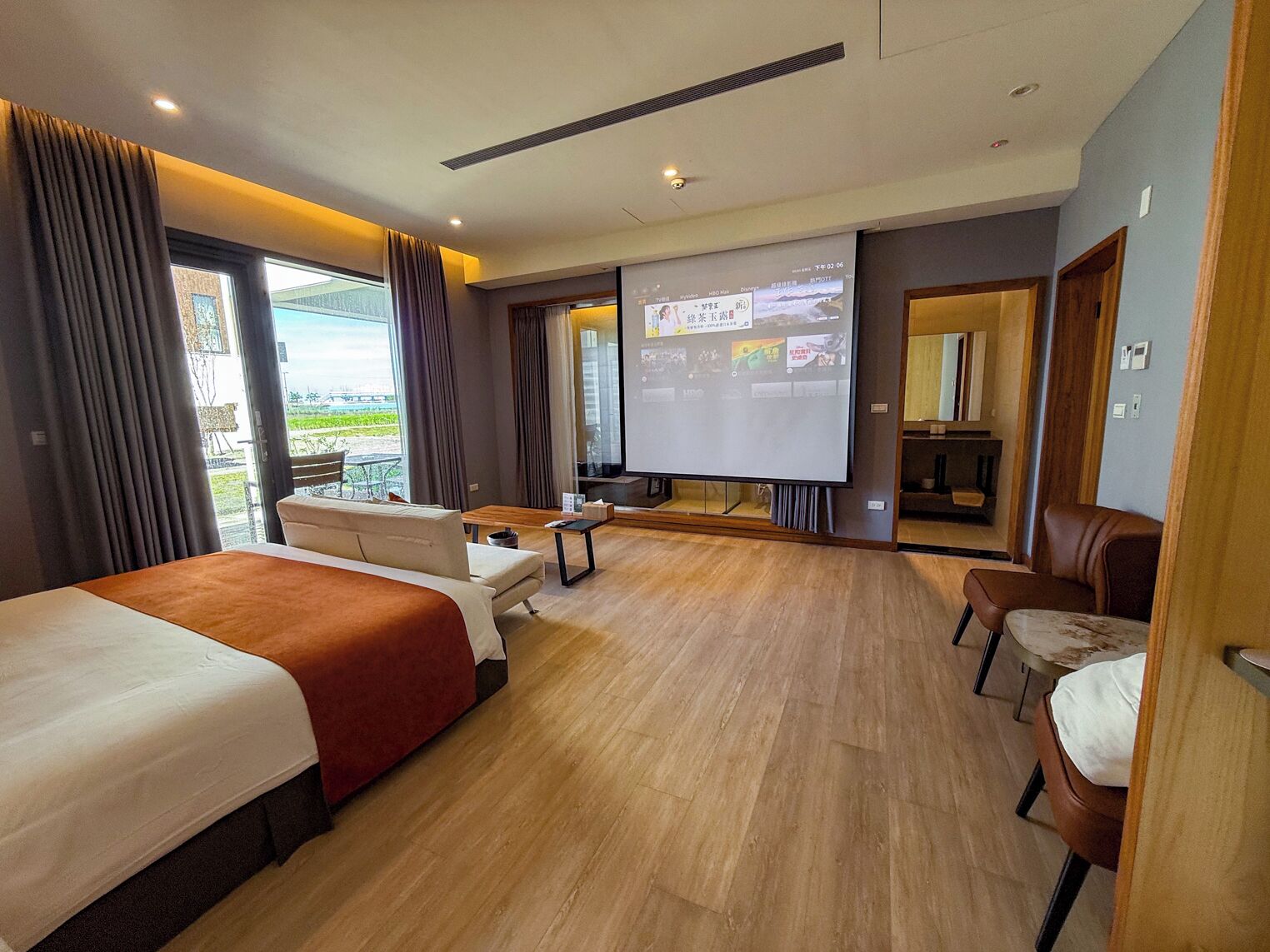 A hotel room with a large bed, a sofa, a TV, and a balcony with curtains.