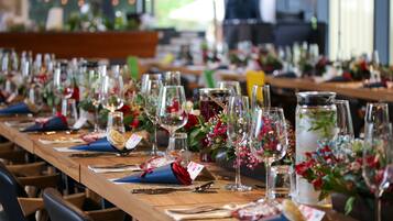 Una larga mesa de comedor dispuesta con varios vasos de vino, cubiertos y centros de mesa florales.