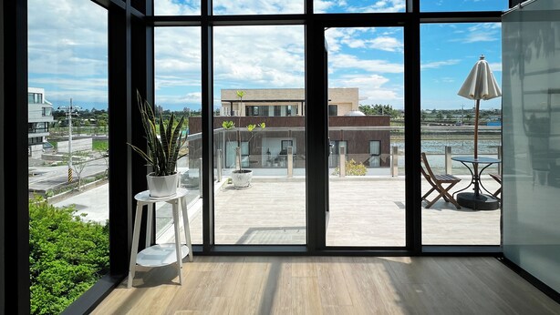 A modern room with large windows, a potted plant, and a view of a building and a body of water. - Villa Loherb (Dongshan)