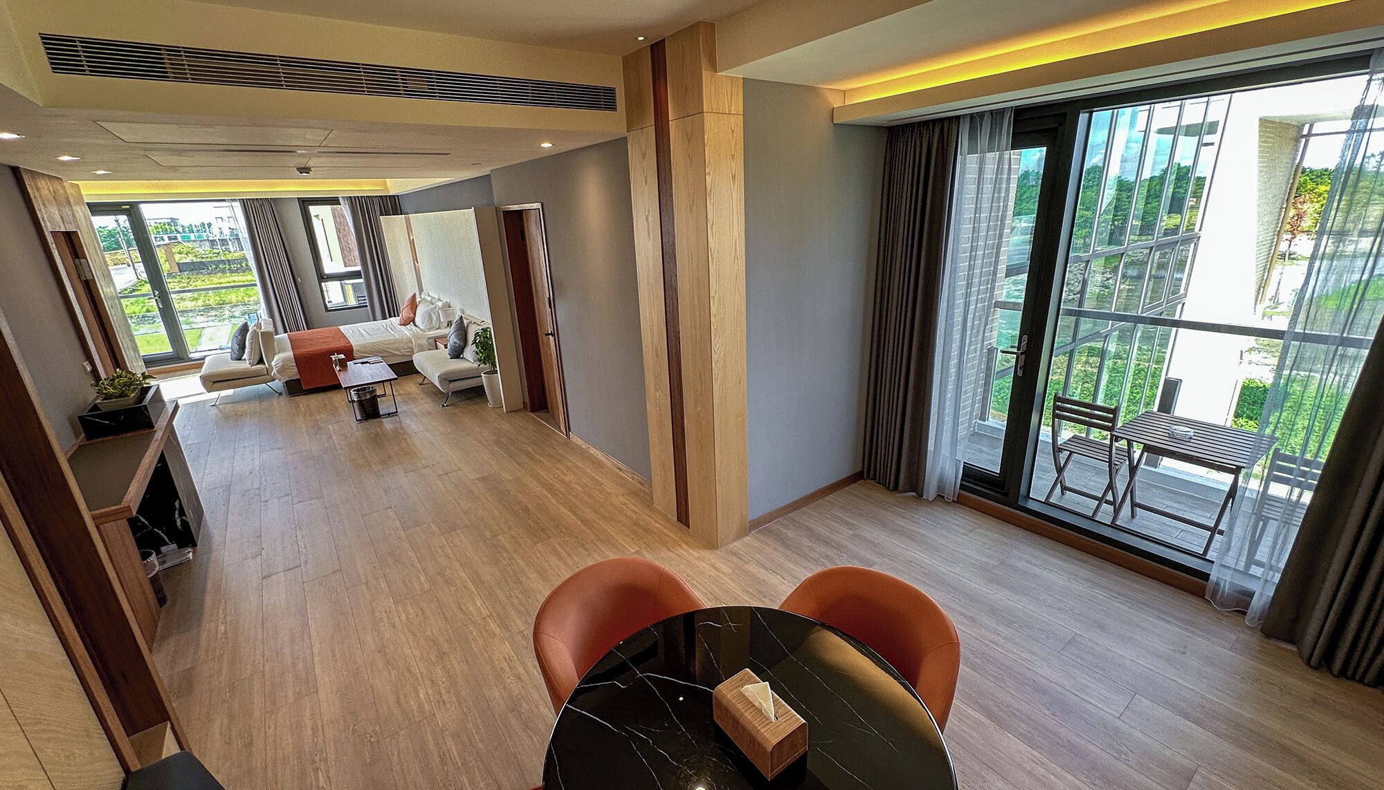 Una habitación de hotel moderna con un balcón grande, un sofá, una mesa de comedor y una pequeña cocina.