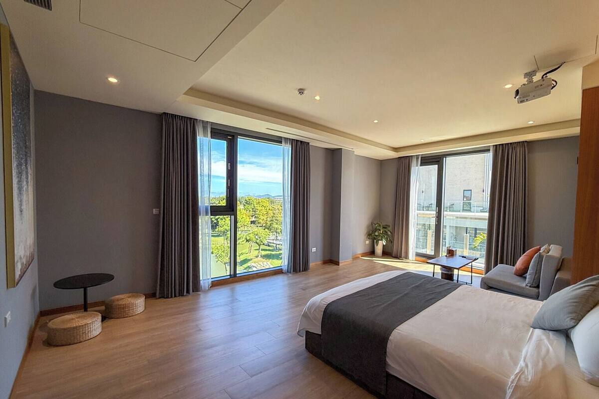 Une chambre d’hôtel moderne avec un grand lit, un balcon offrant une belle vue et une petite table agrémentée d’une plante.