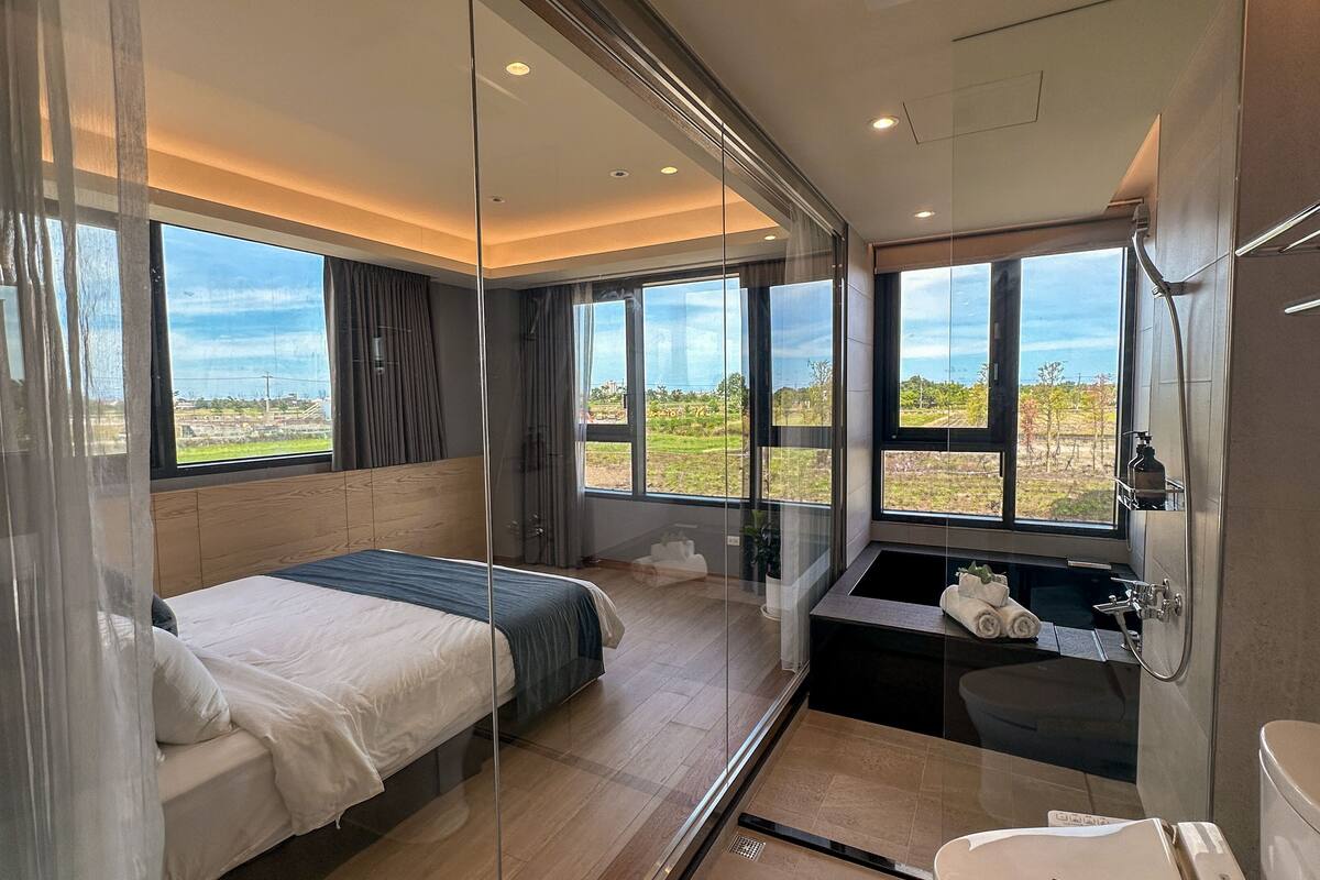 Une chambre moderne avec un grand lit, une douche en verre et une vue sur la campagne.