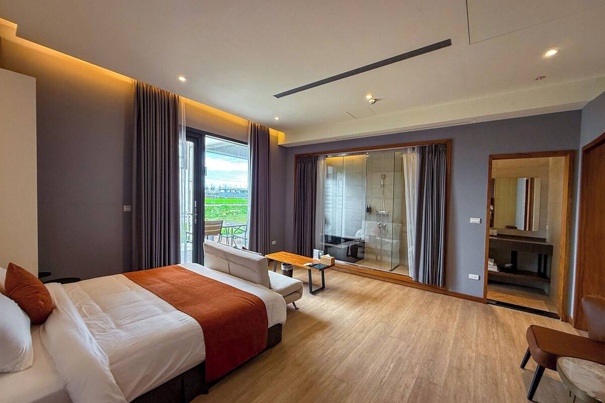 Une chambre d’hôtel moderne dotée d’un grand lit, d’un bureau et d’une salle de bain avec une douche en verre.