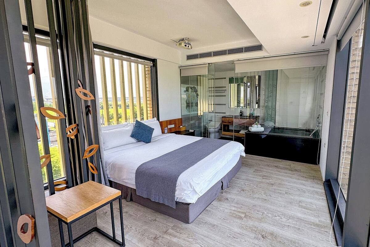 Une chambre d’hôtel moderne dotée d’un grand lit, d’un bureau et d’une salle de bain avec une douche en verre.