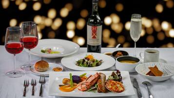 Una mesa servida con diversos platos, entre ellos mariscos, verduras y un postre, junto con copas de vino y una botella.
