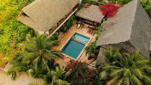 An aerial view of a resort with thatched-roof buildings, a swimming pool, and lush tropical vegetation. - Tamani Villas Annex (Matemwe)