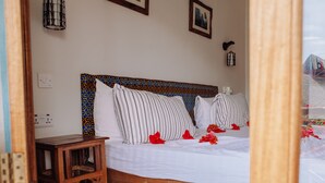 A bedroom with a wooden bed, striped pillows, and a small wooden table. - Tamani Villas Annex (Matemwe)