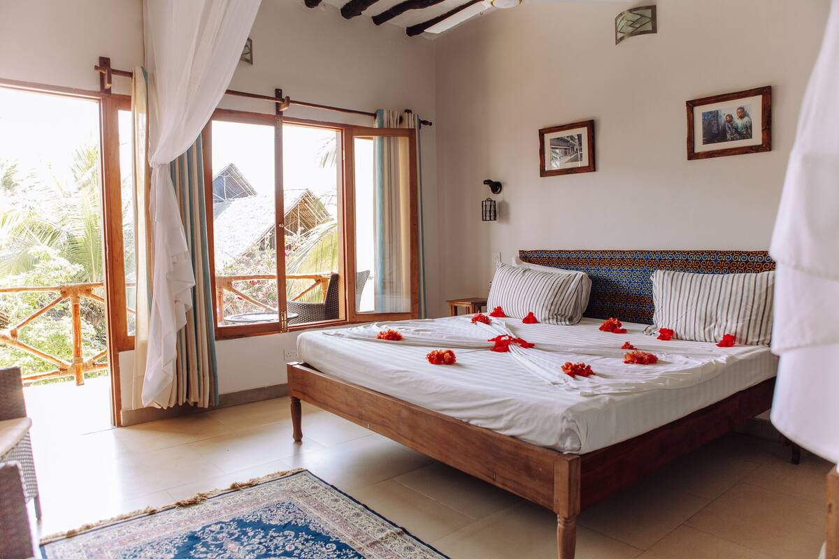 Un dormitorio con cama de madera, un ventanal con cortinas y vistas a zonas verdes, además de una alfombra estampada en el suelo.