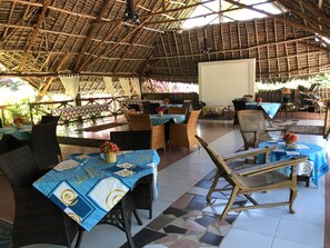 An outdoor dining area with thatched roof, wicker furniture, and tiled flooring. - Tamani Villas Annex (Matemwe)
