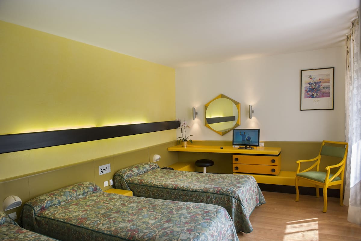 A hotel room with two single beds, a desk with a chair, a mirror, and a framed picture on the wall.