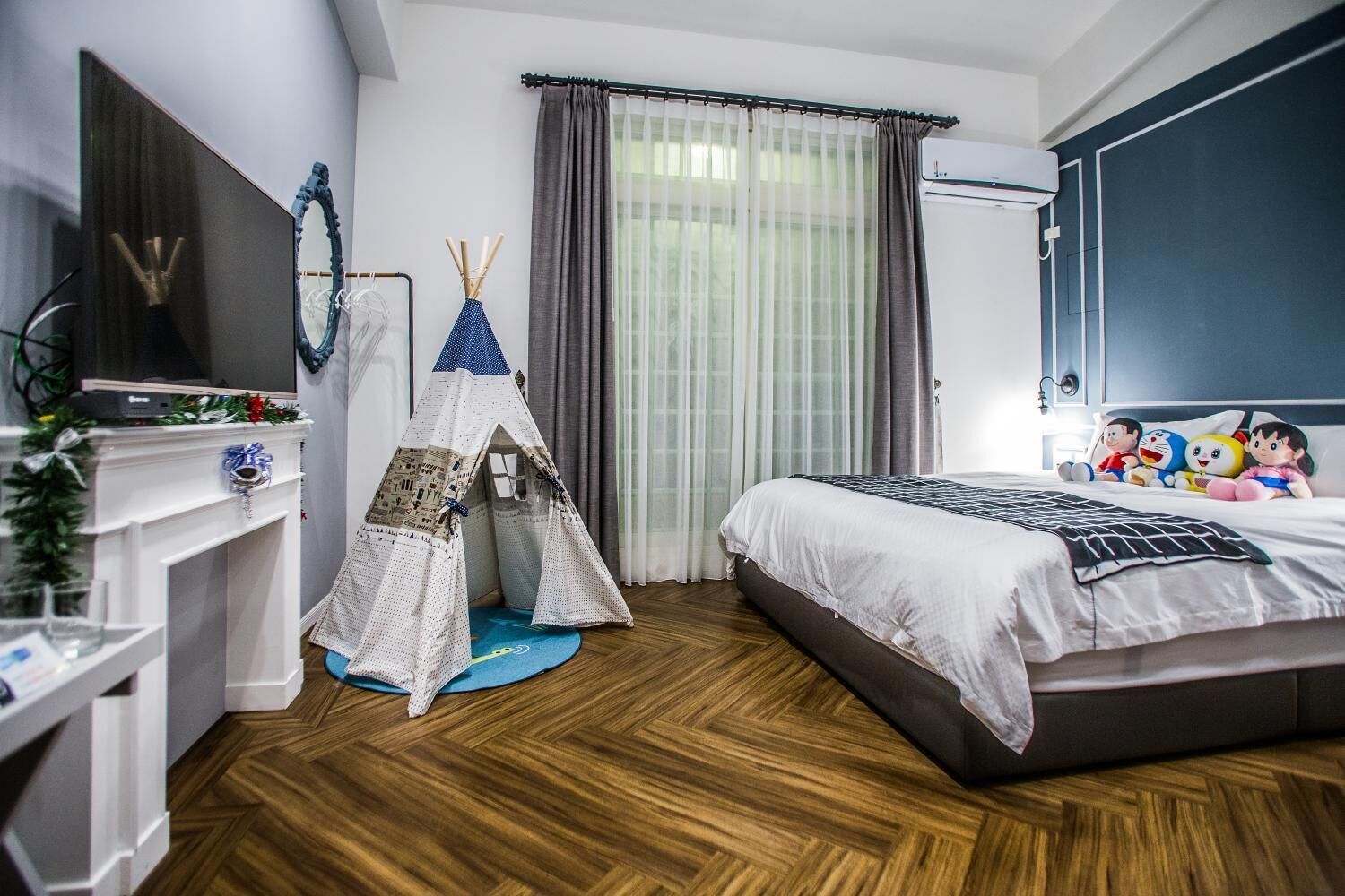 Quarto com cama, cômoda, televisão, janela com cortinas e uma estrutura semelhante a uma tenda.