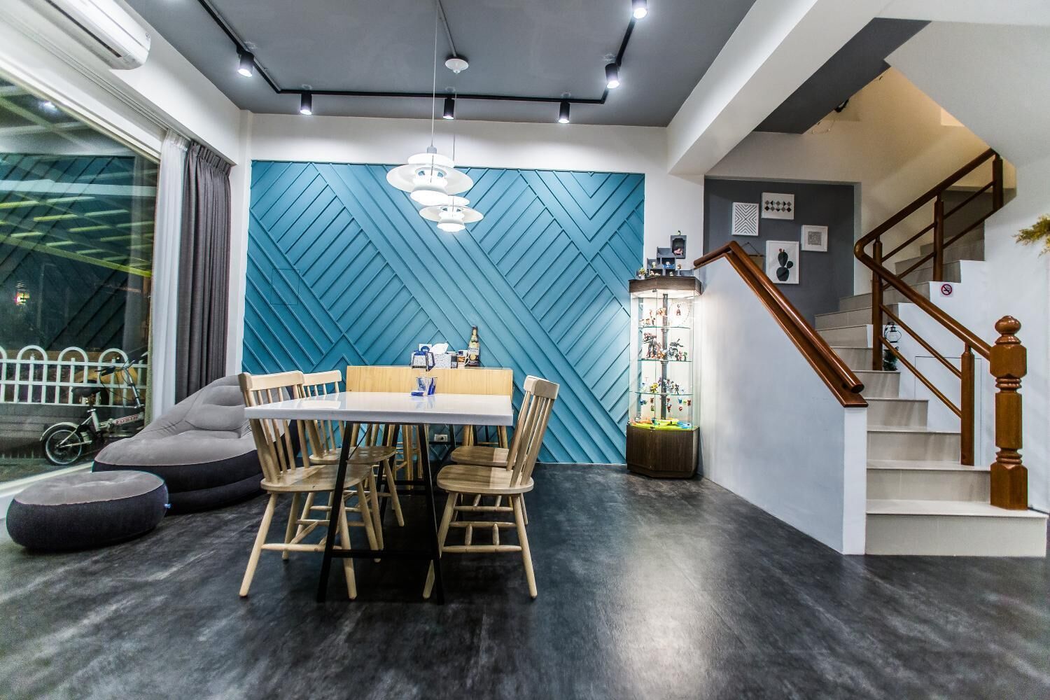 Un comedor moderno con una pared azul con motivos geométricos, una mesa de comedor de madera con sillas y una escalera con barandilla de madera.