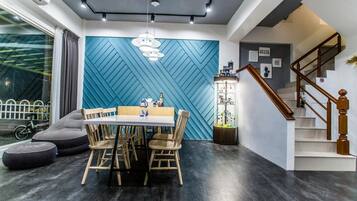 Un comedor moderno con una pared azul con motivos geométricos, una mesa de comedor de madera con sillas y una escalera con barandilla de madera.