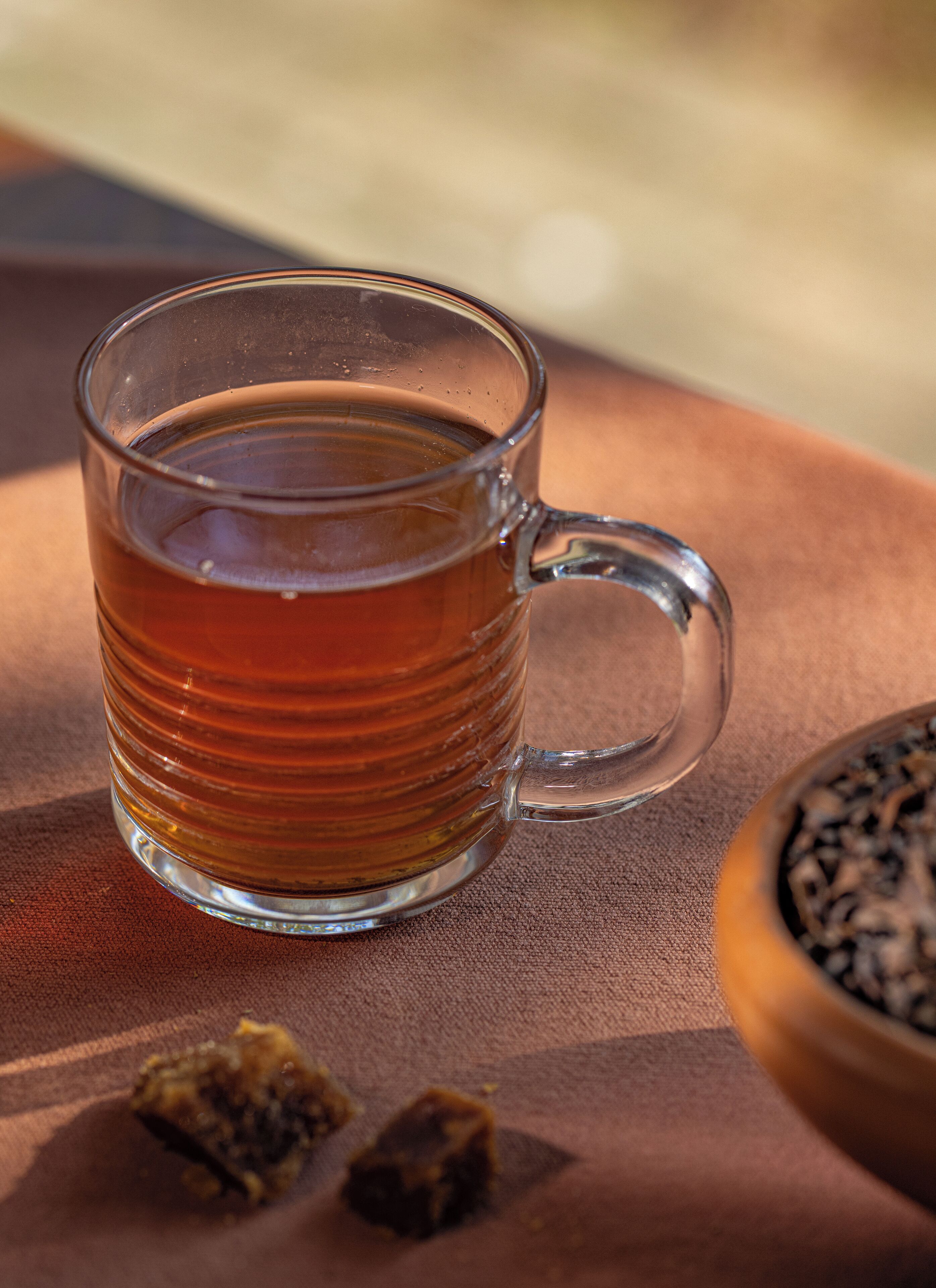 A clear glass mug filled with a brown liquid, placed on a textured surface with a blurred background.