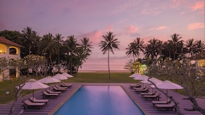 A pool area with lounge chairs and umbrellas, surrounded by palm trees and a view of the ocean at dusk. - Heritance Ayurveda (Beruwala)
