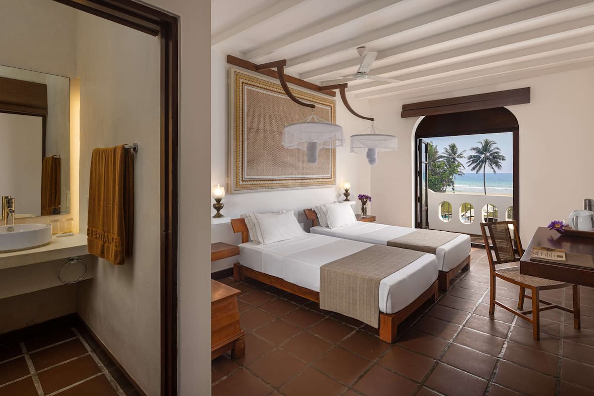 A hotel room with two beds, a bathroom with a sink, and a view of the beach.