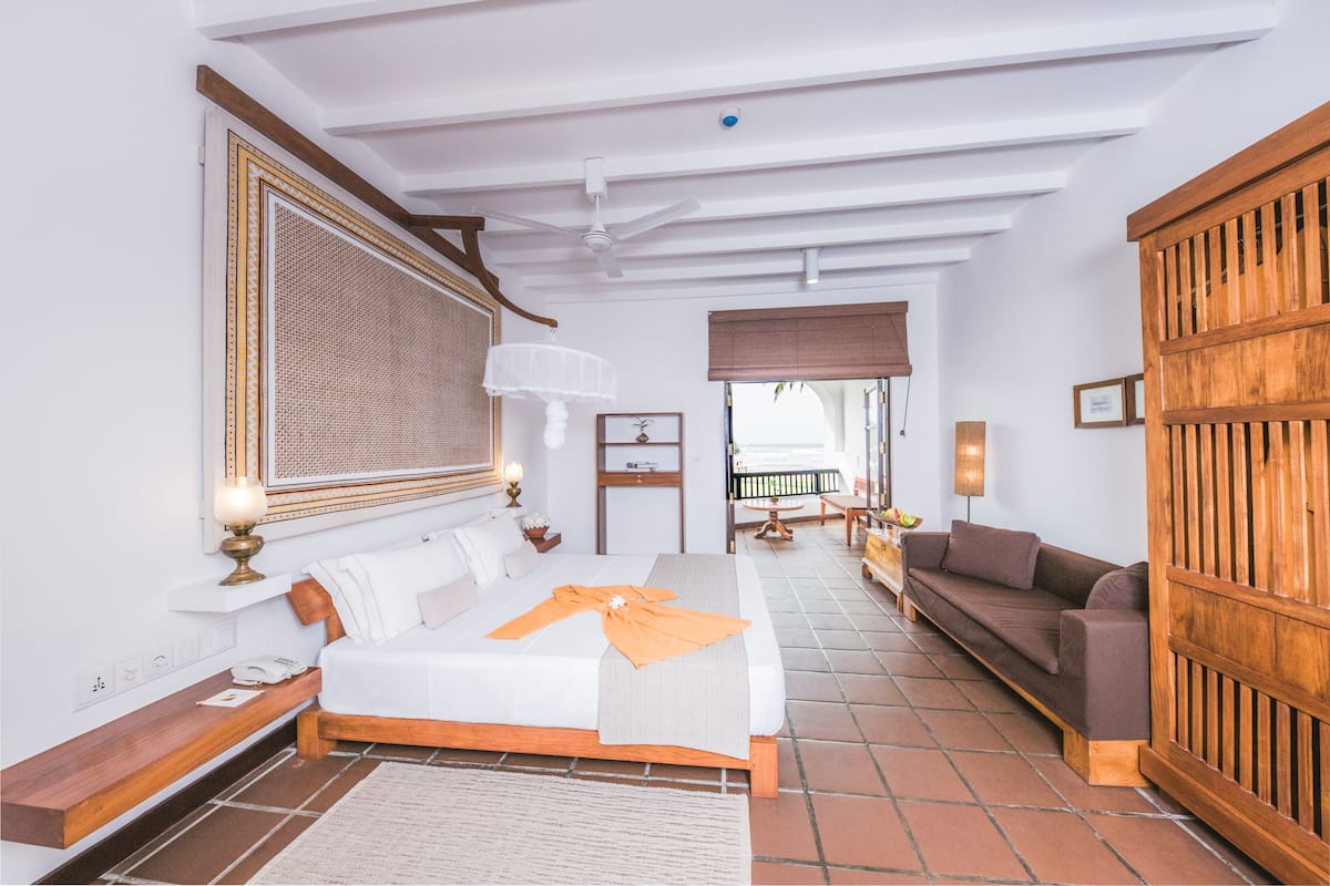 A hotel room with a bed, a wooden bench, a sofa, and a large wooden partition.