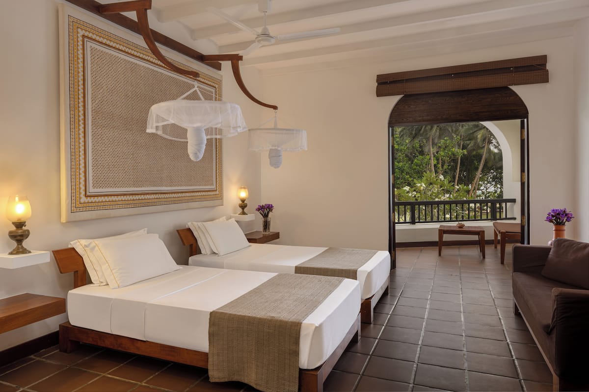 A hotel room with two beds, a balcony, and a view of greenery.