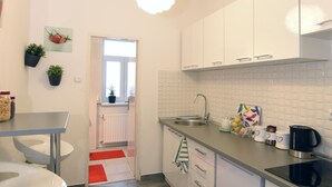 Een moderne keuken met witte kasten, een roestvrijstalen spoelbak en een zwarte koffiezetapparaat. Er is een raam boven de spoelbak en een rood kleed dat naar een deur leidt.