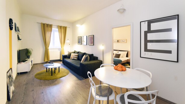 Een moderne woonkamer met een bank, een eettafel met stoelen, een televisie en een groot kunstwerk in een lijst aan de muur.