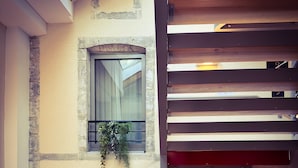 A multi-story building with a balcony, a window with a curtain, and a wall-mounted light fixture.