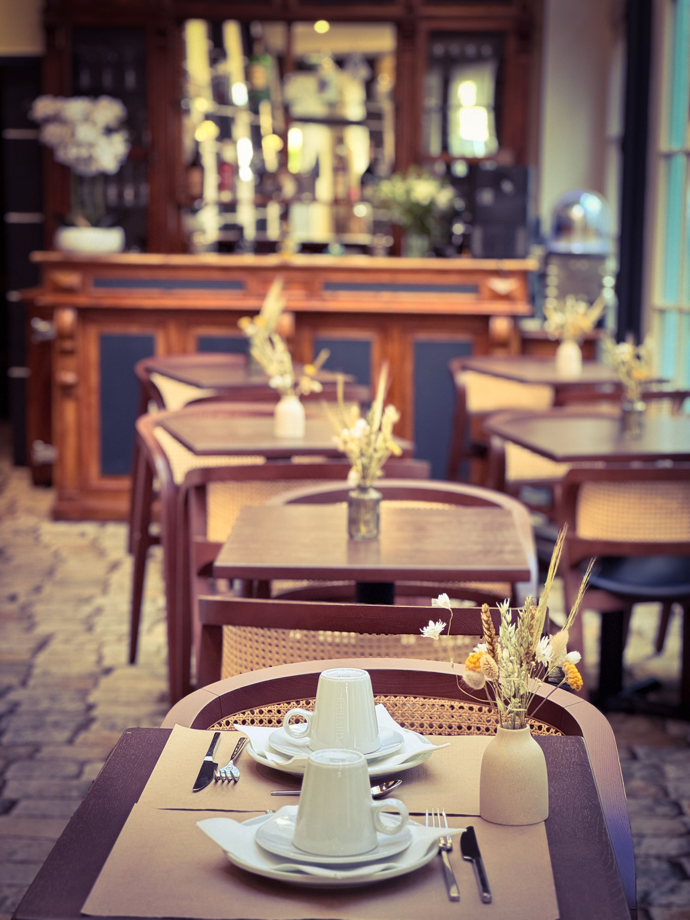 Un restaurant amb taules i caires de fusta, una barra al fons i un ram de flors sobre la taula.