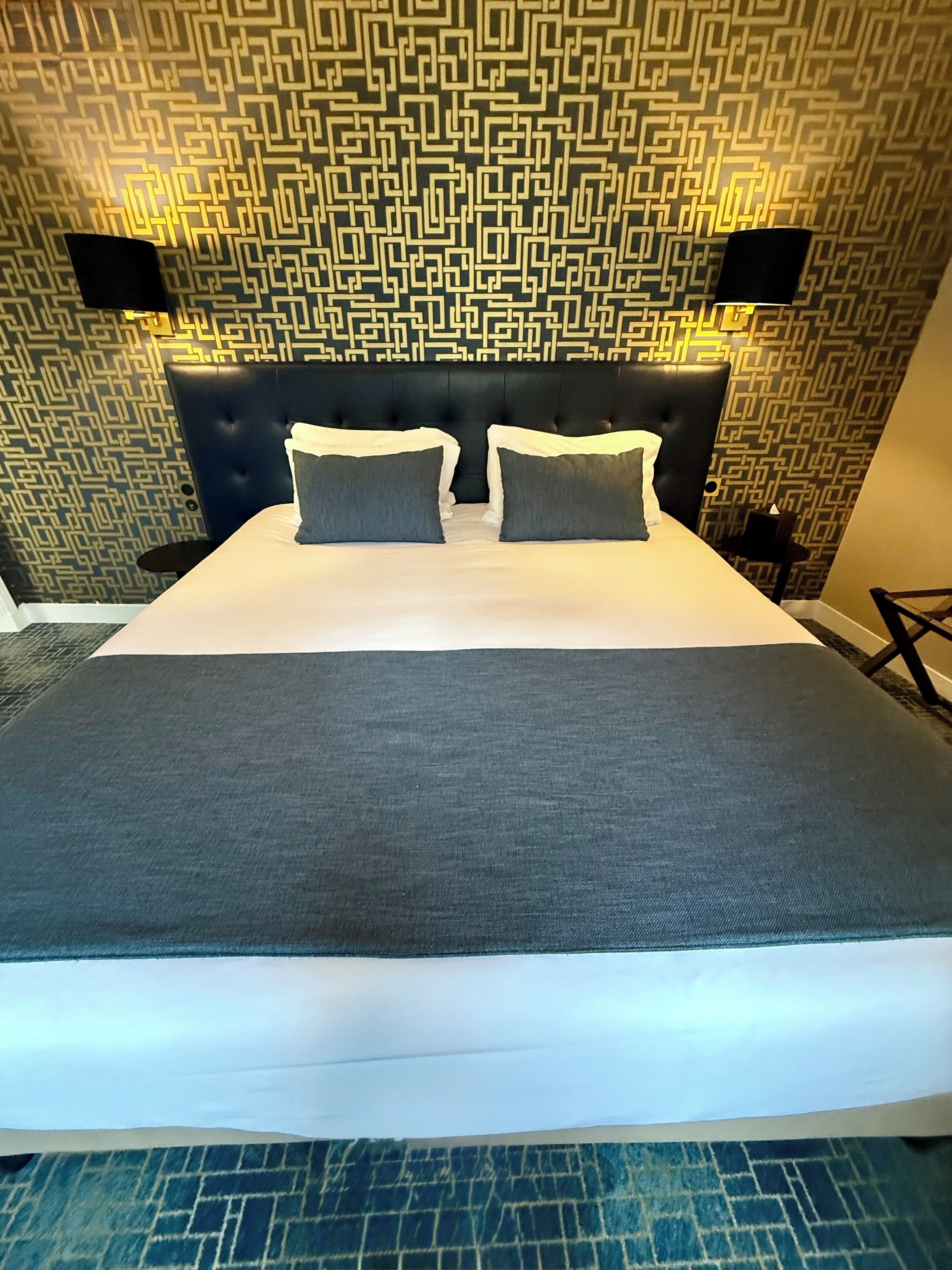 A hotel room with a large bed, a patterned wall, and a black headboard.