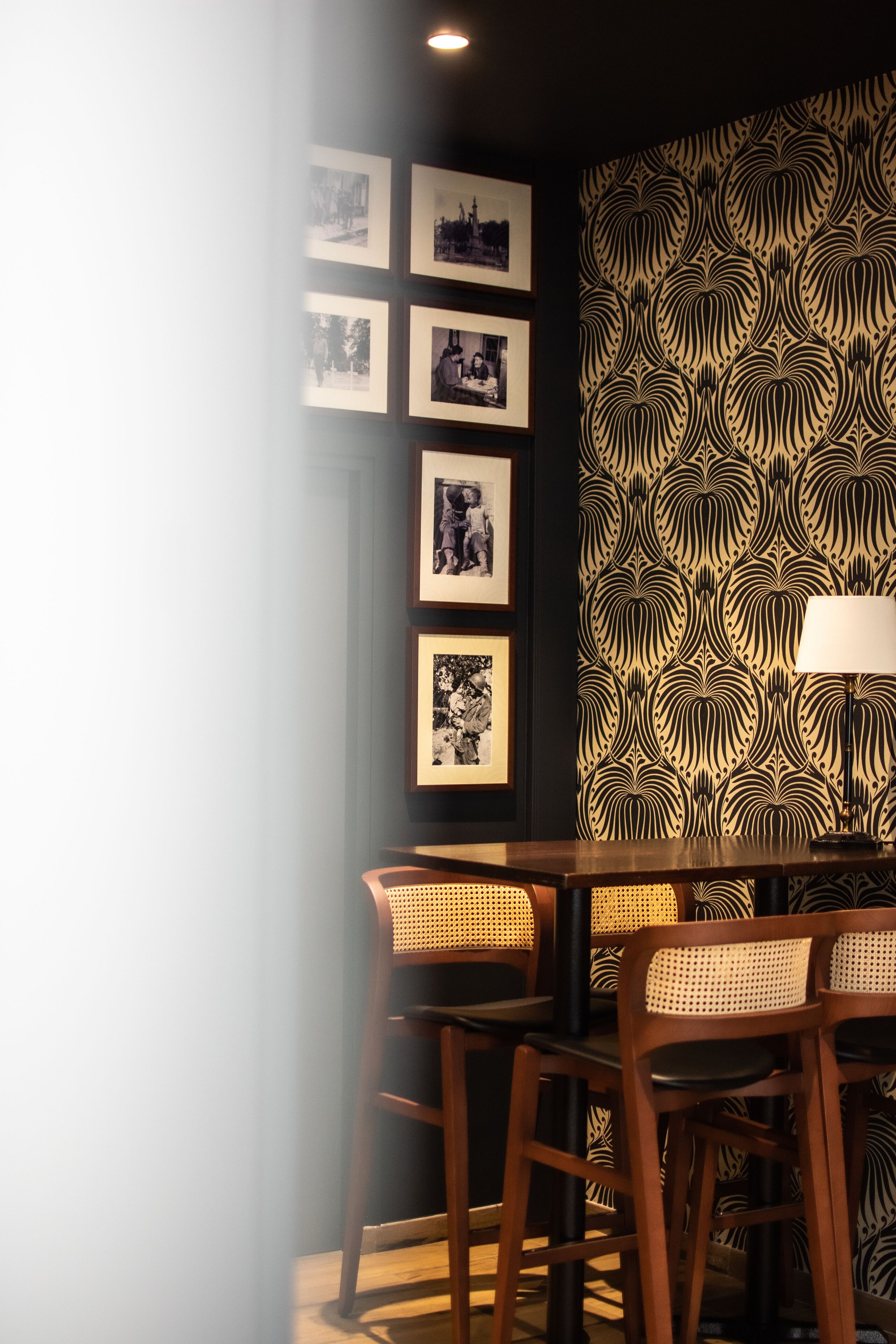 A dining area with a wooden table and chairs, framed photographs on the wall, and a patterned wallpaper.