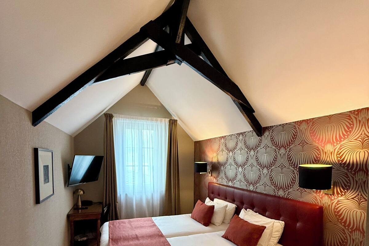 Hotelkamer met een groot bed, bureau, stoel, televisie en een behang met patroon.