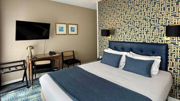 Een hotelkamer met een groot bed, een bureau met lamp, een televisie en een behang met een patroon.