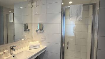 A modern bathroom with a large mirror, a white sink, a shower enclosure, and a towel rack.