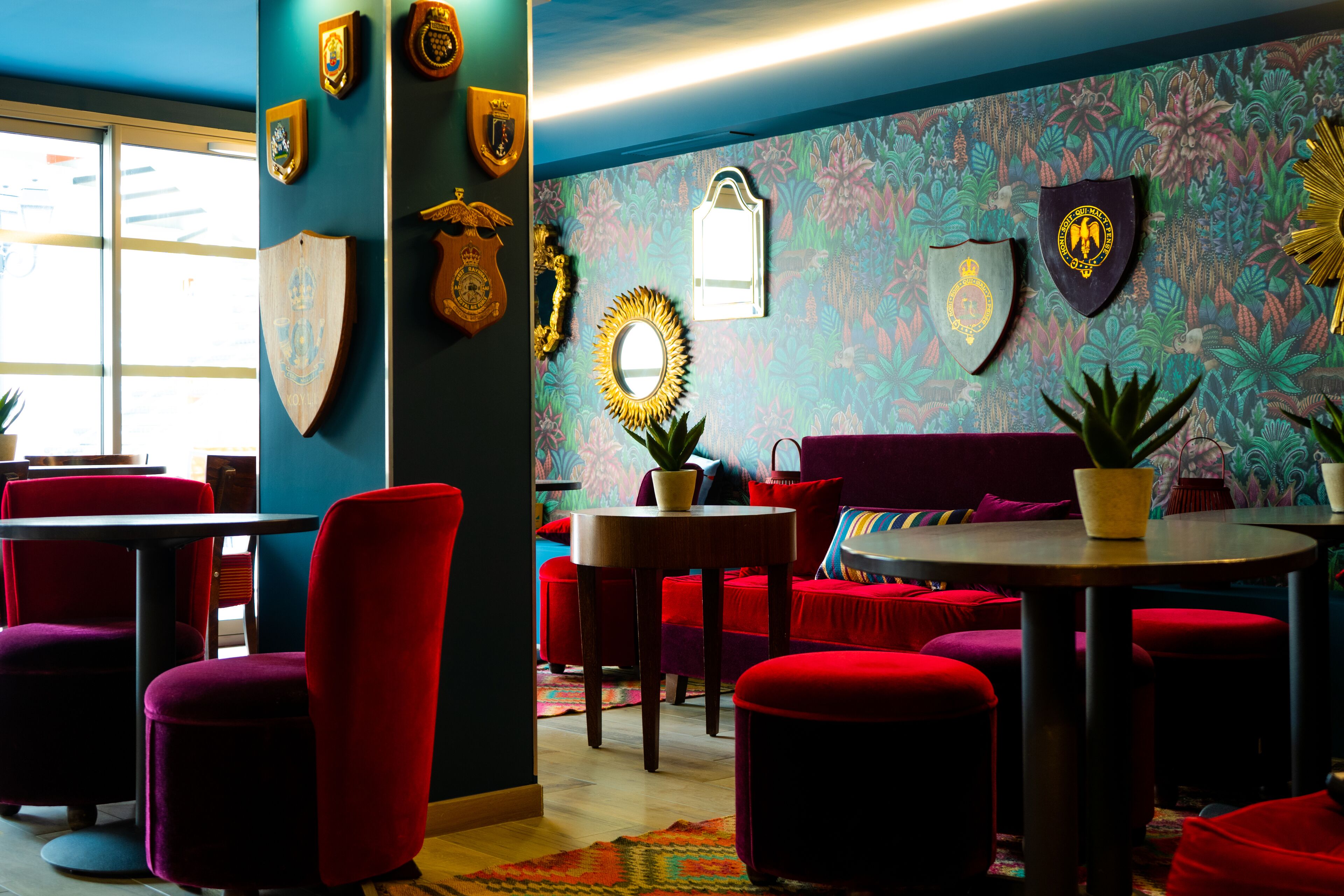A room with red upholstered seating, a round table, and decorative shields on the wall.