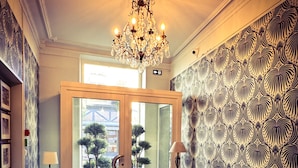 A room with a chandelier, patterned wallpaper, a black sofa, and a view of the outside through a glass door.