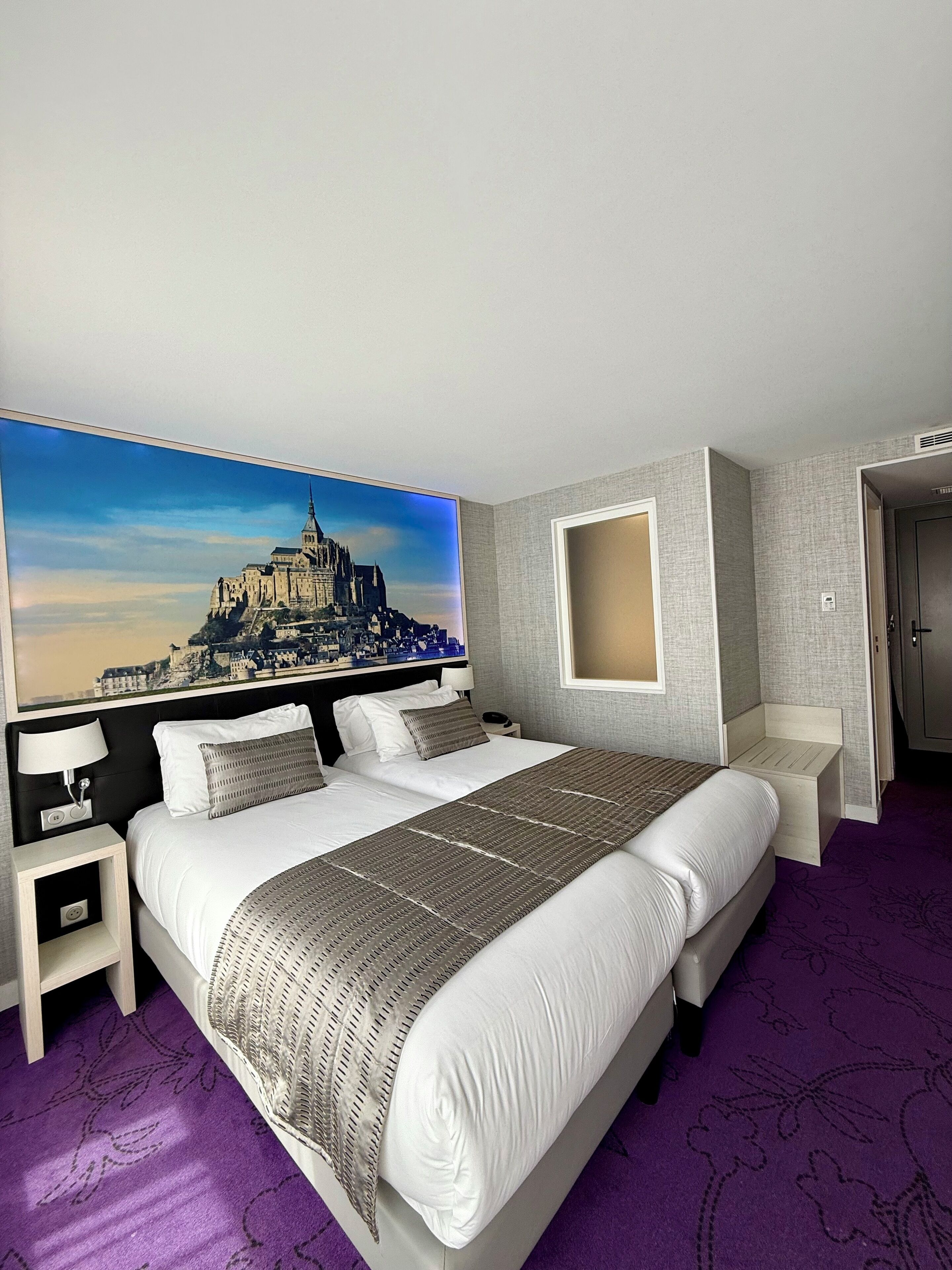 Une chambre d’hôtel avec un grand lit, une table de chevet, un téléviseur fixé au mur et une porte.