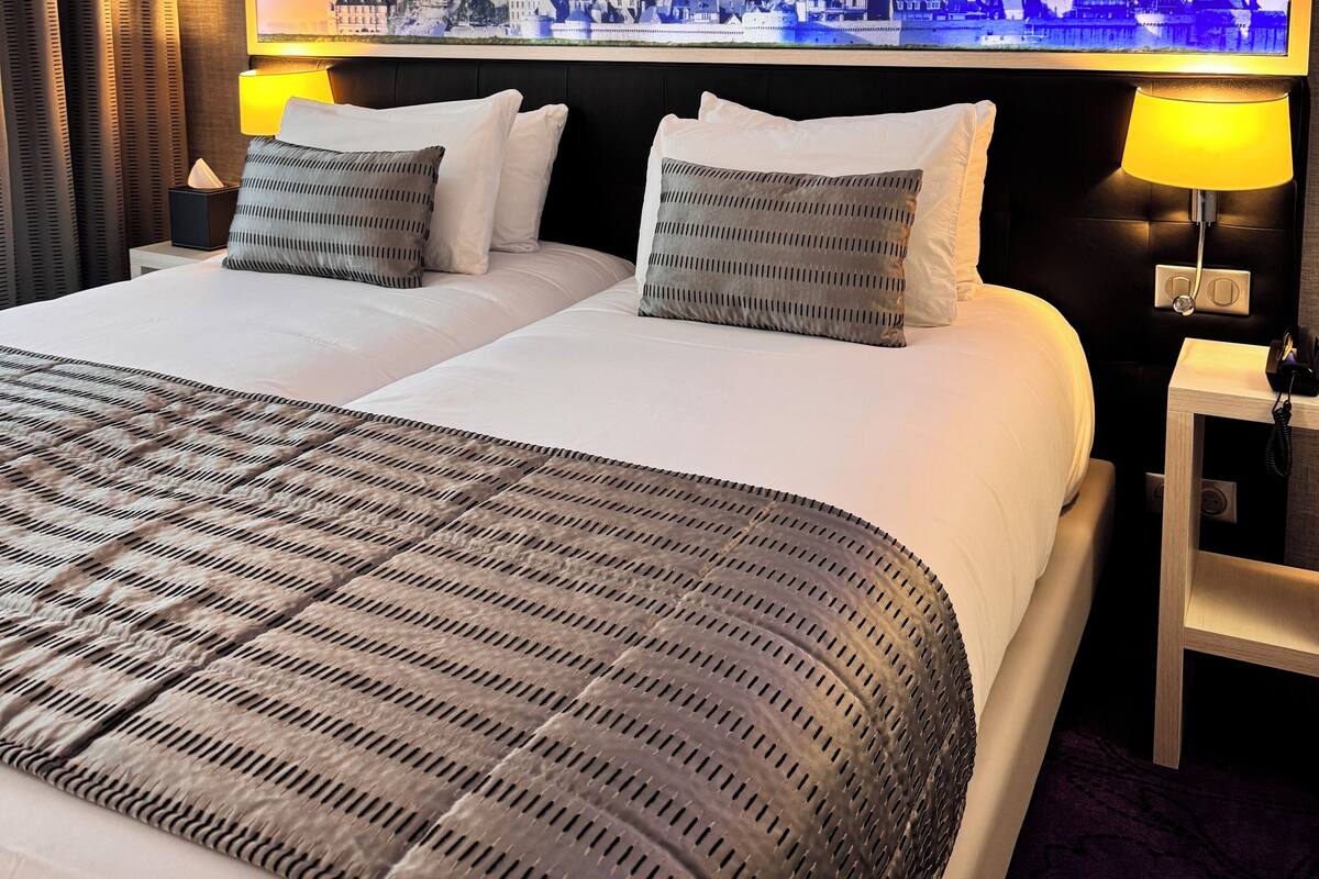 A hotel room with a large bed, two bedside lamps, a nightstand, and a large framed picture of a historic building.