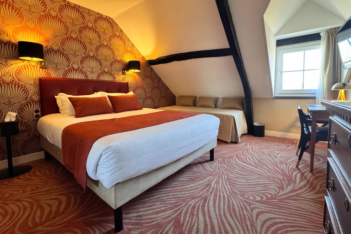 A bedroom with a large bed, a smaller bed, a desk, and a window.