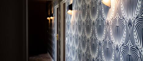 Un pasillo con papel tapiz estampado y luminarias fijadas a la pared.