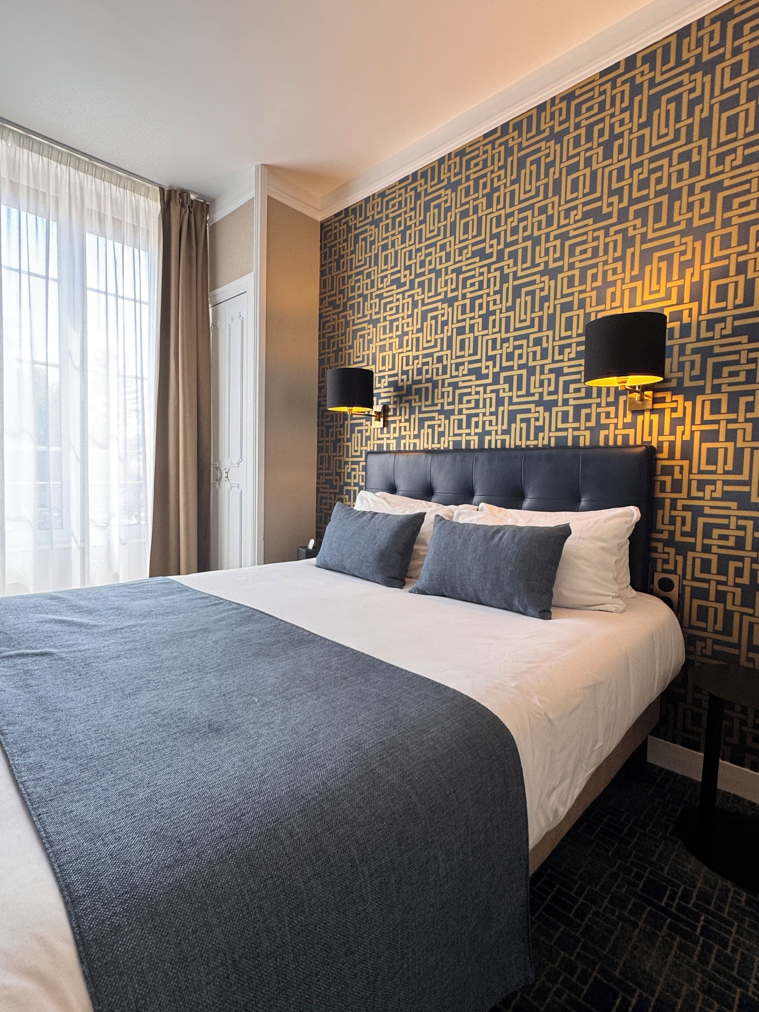 Een hotelkamer met een groot bed, een patroonmuur en twee wandlampen.