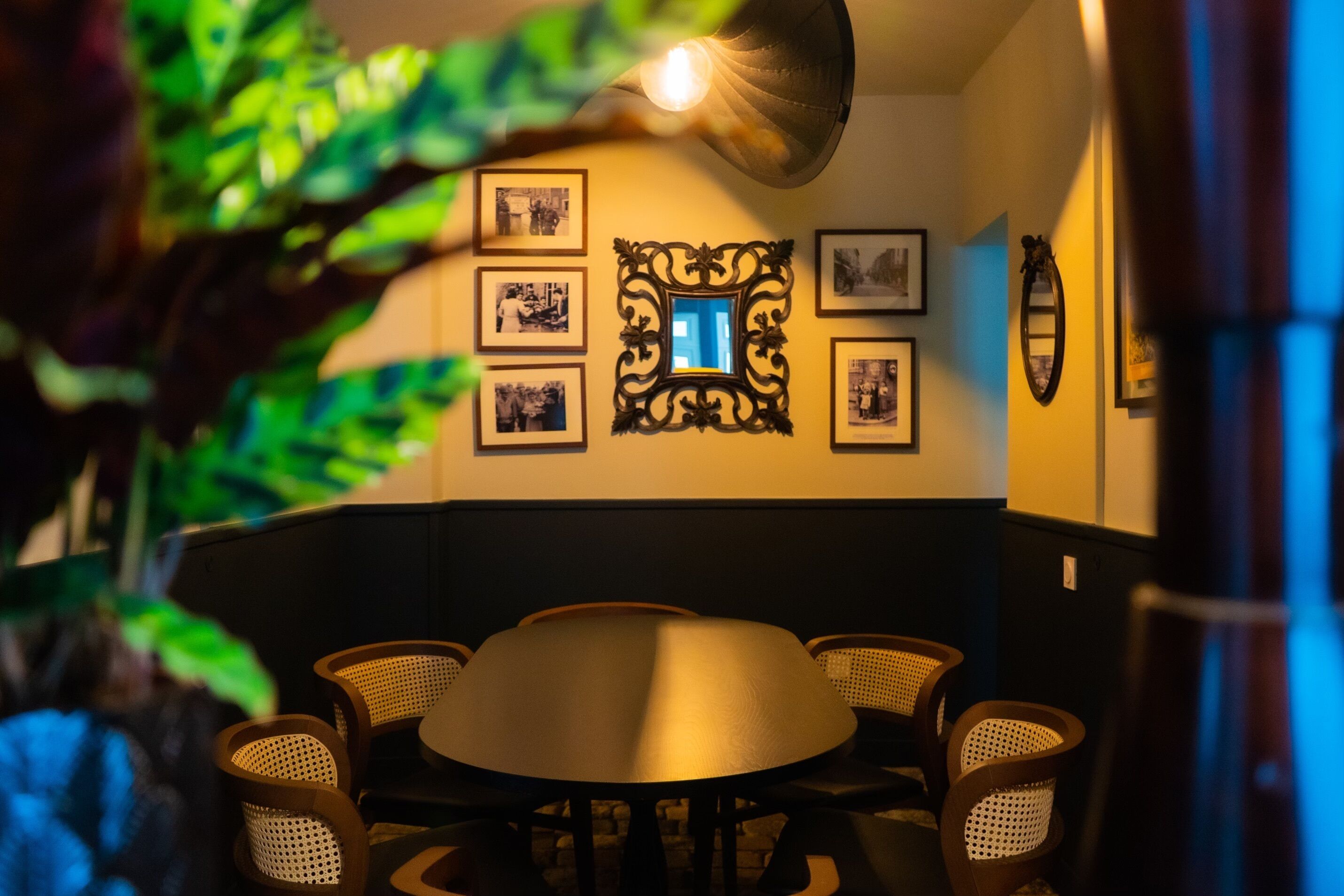 A dining area with a round table surrounded by wicker chairs, a wall-mounted mirror, and framed photographs.