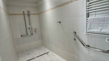 A modern bathroom with a shower, toilet, and handrails.