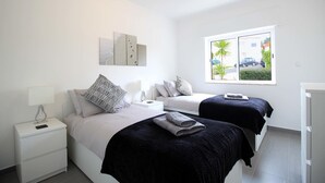 A bedroom with two beds, a nightstand, a lamp, and a window with a view of the outside. - Casa Scarlett, Walk to beach, Communal Pool (Carvoeiro)
